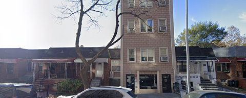 A street view of a residential area with a two-story building and cars parked in front.