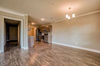 A large empty room with wooden floors and a kitchen area in the background at Mode at Melbourne, LLC Apartments, Melbourne, Florida