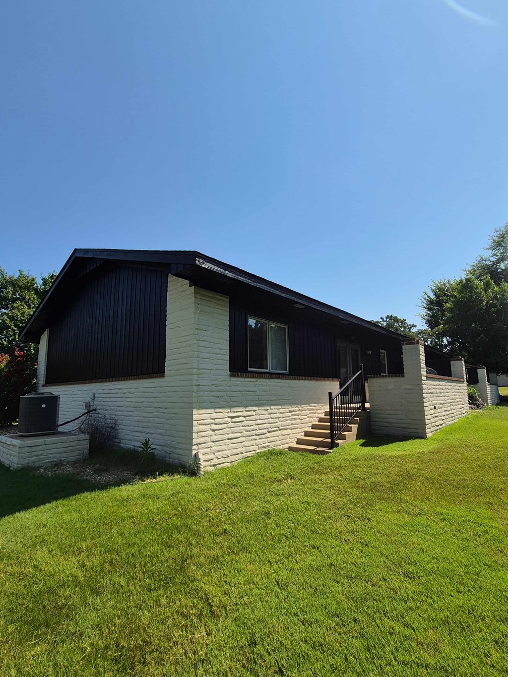 A house with a black roof and white siding is surrounded by a grassy lawn.