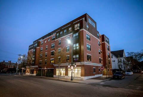 A large red brick building with a lit up window on the second floor.