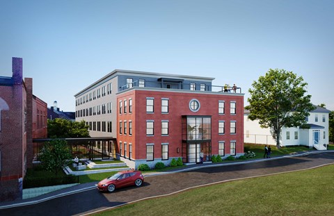 A red car is parked on the street in front of a red brick building.