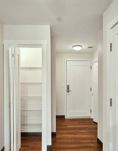 A white door is open to a hallway with wood floors.