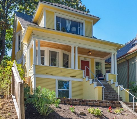 A yellow house with a red door and a staircase leading to the entrance.