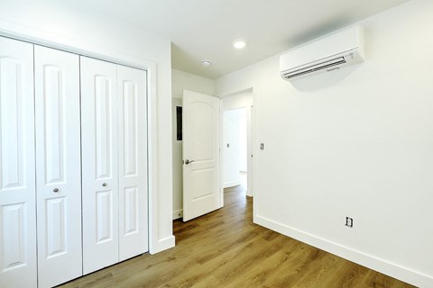 A white room with a wood floor and a wall-mounted air conditioner.