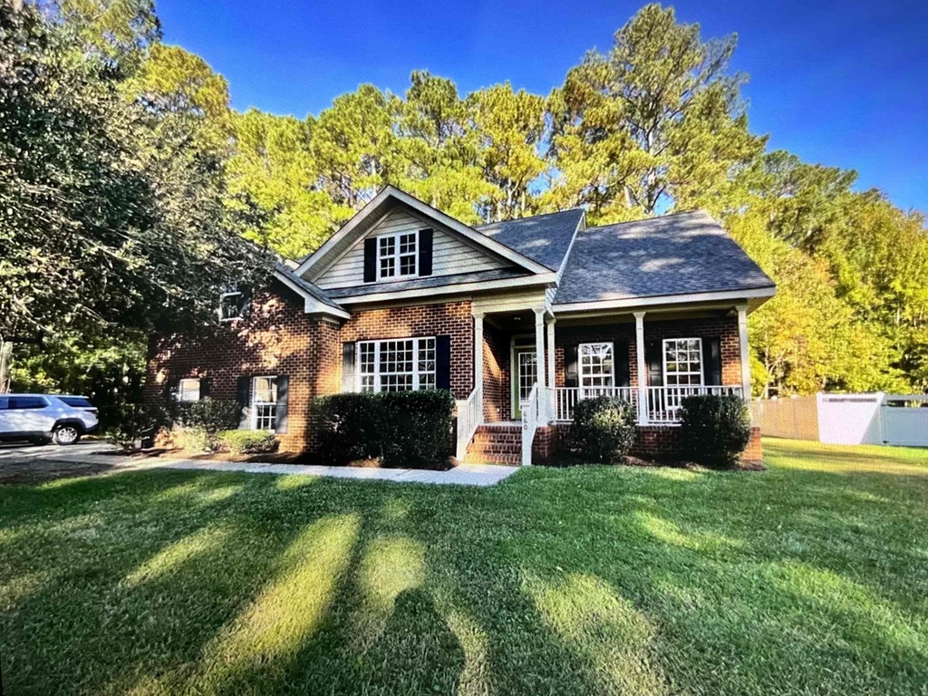 A house with a white porch and a brick exterior sits in a grassy front yard.