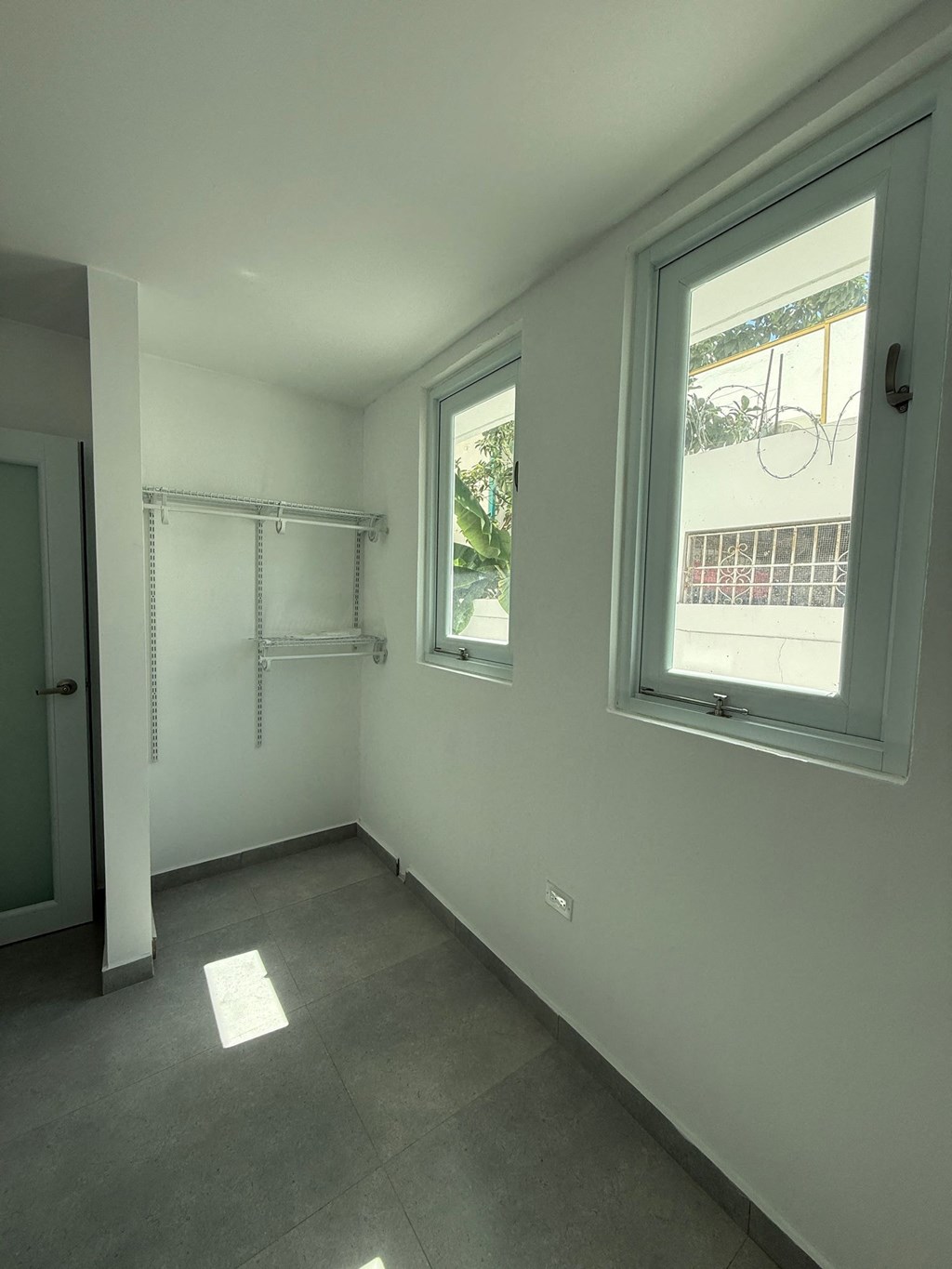 A room with a grey floor and a window showing a balcony.