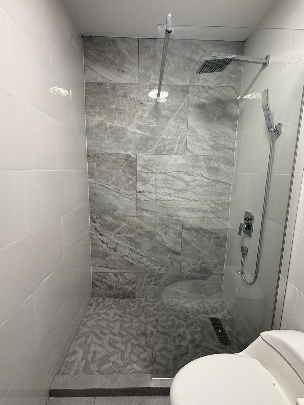 A bathroom with a marble tile shower and a white toilet.