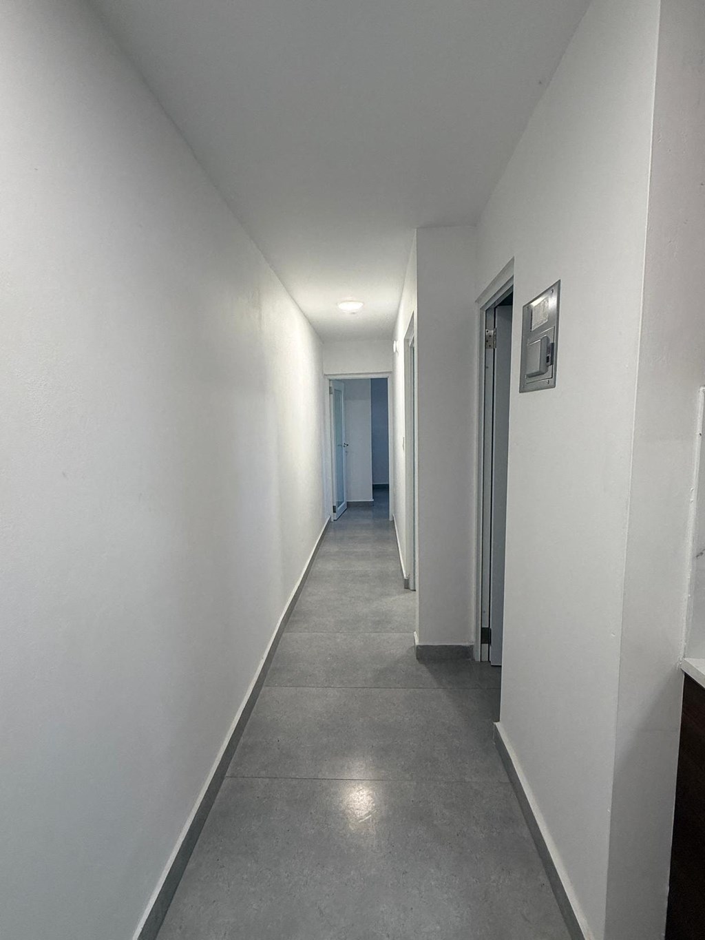 A long, narrow hallway with white walls and grey flooring.