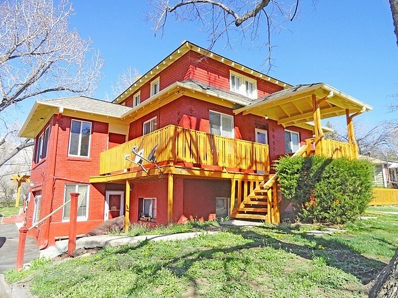 A red and yellow house with a balcony and stairs leading to the front door.