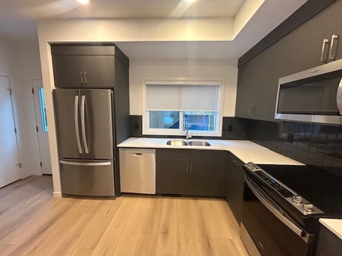 A modern kitchen with a stainless steel refrigerator and wooden flooring.