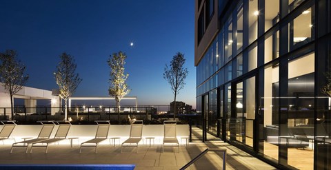 A modern building with a pool and lounge chairs in front.