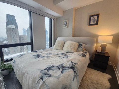 A bedroom with a large bed and a city view through the window.