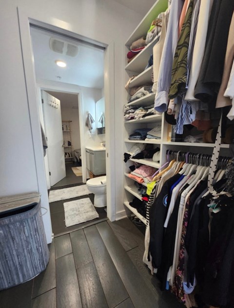 A walk in closet with clothes on shelves and a mirror.