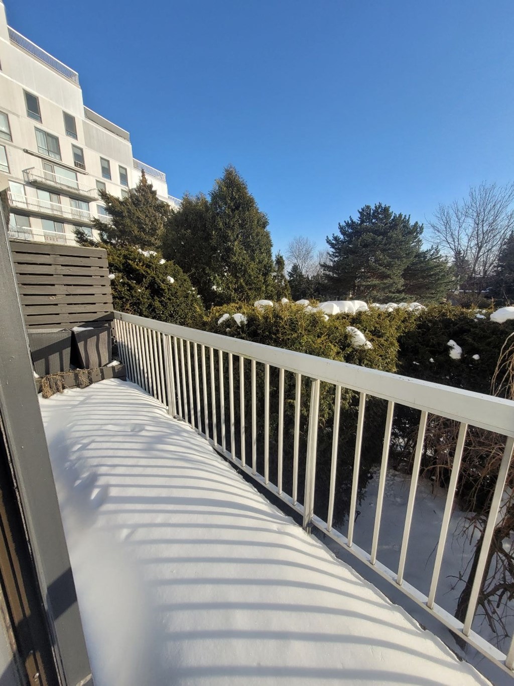A white railing on a balcony with a building and trees in the background.
