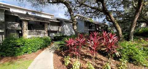 A pathway leads to a building with a balcony and a tree in front.