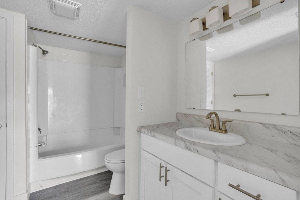 A white bathroom with a marble countertop and a white toilet.
