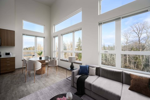 A modern living room with a grey couch and a kitchen area with a microwave.