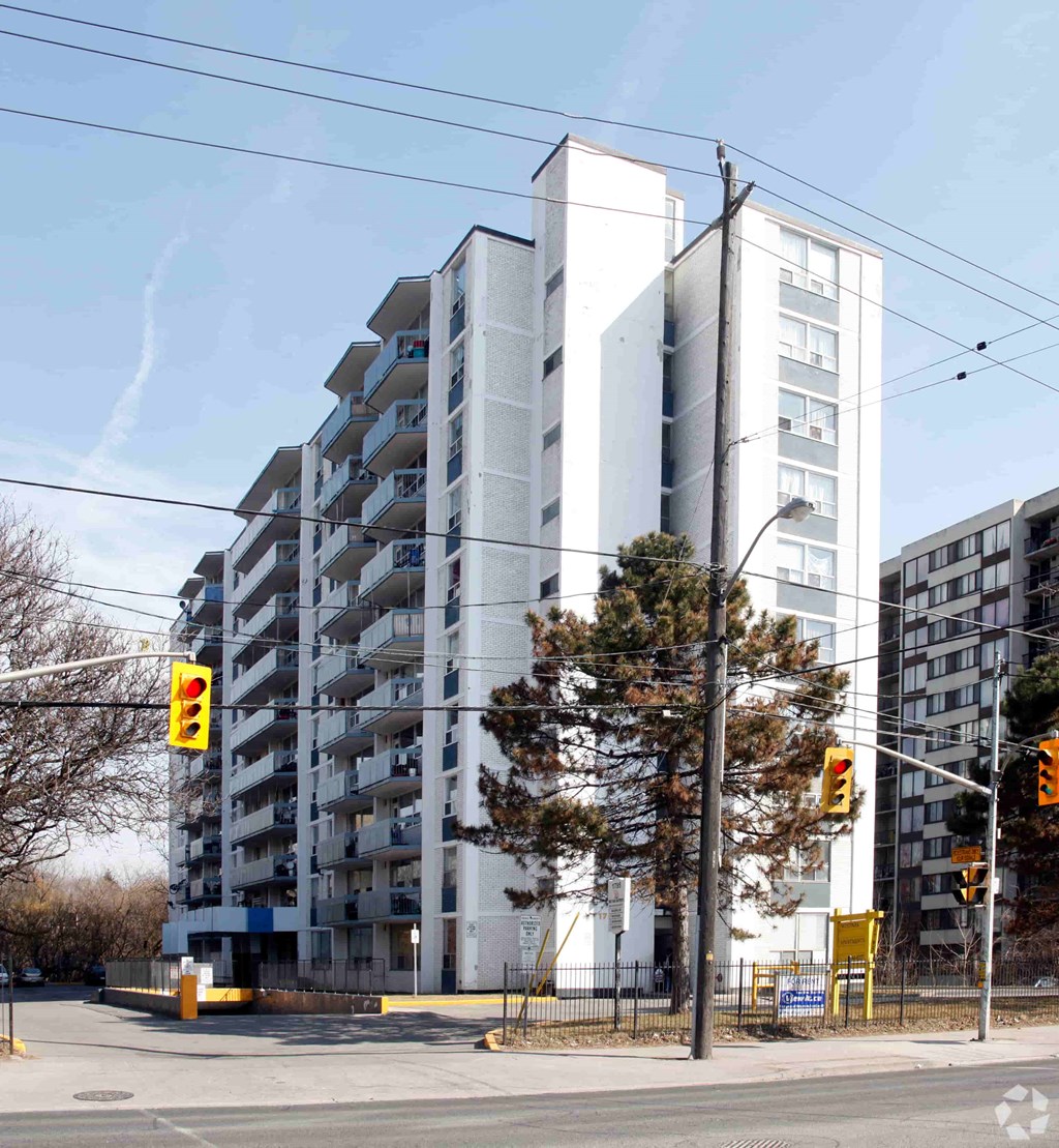 A tall white building with balconies is in the background of a street corner.