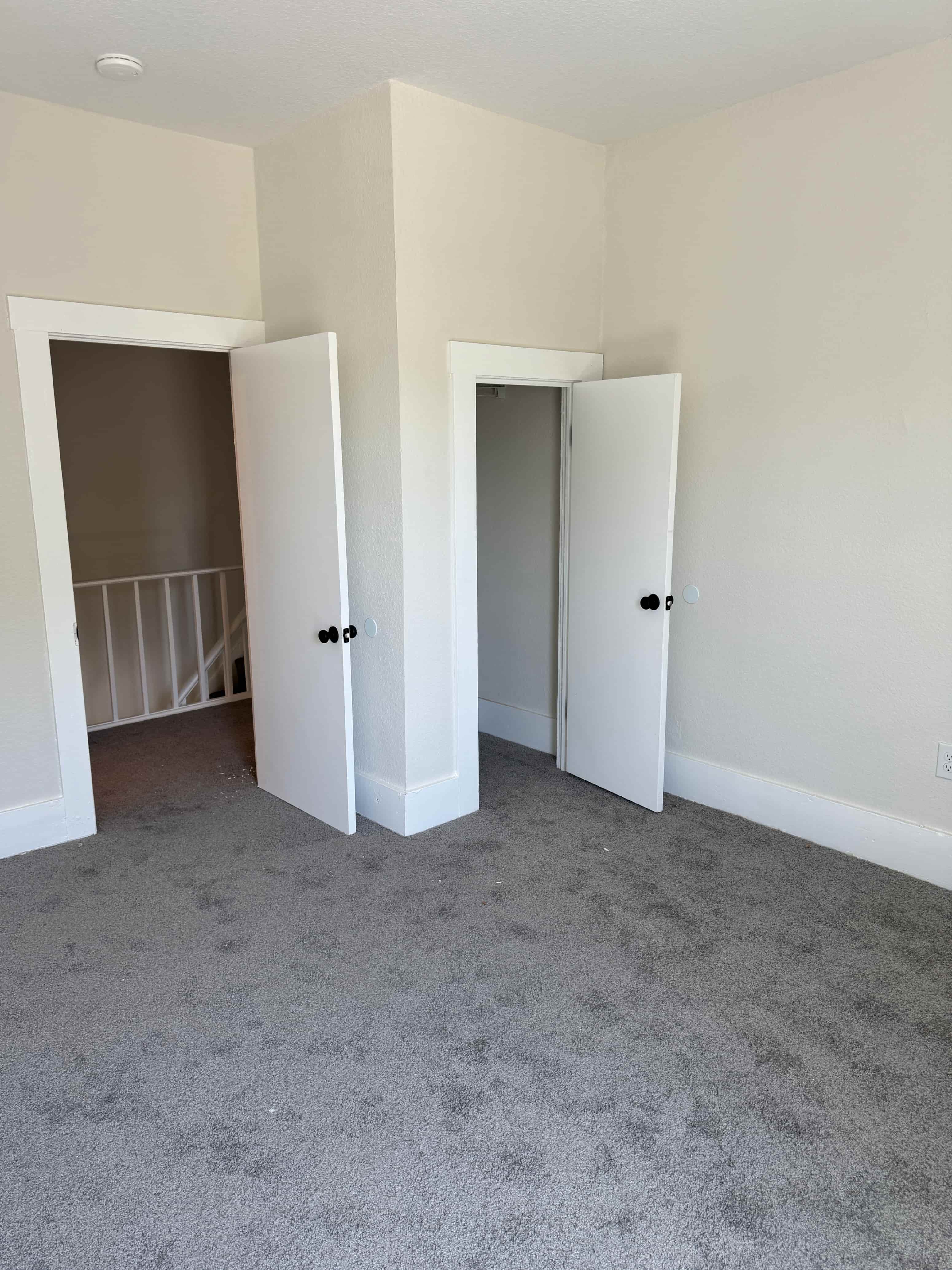 A room with two white doors and a grey carpet.