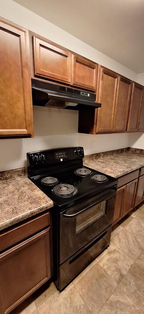 A kitchen with brown cabinets and a black stove top oven.
