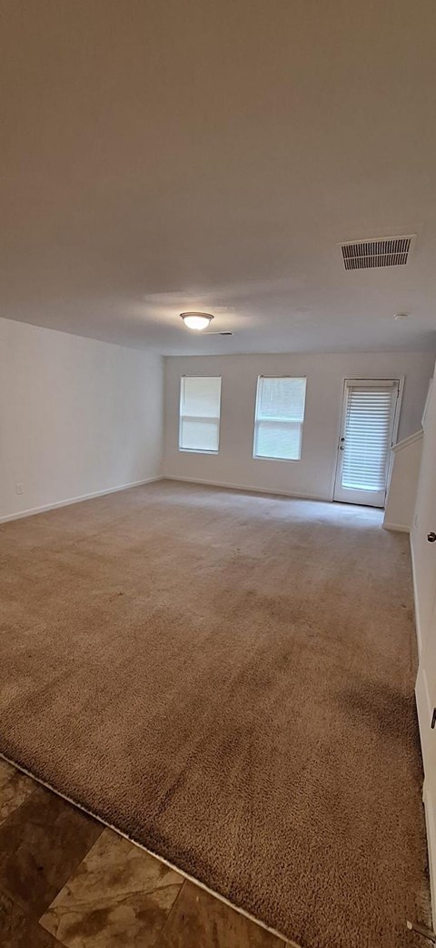 A room with a carpeted floor and two windows.