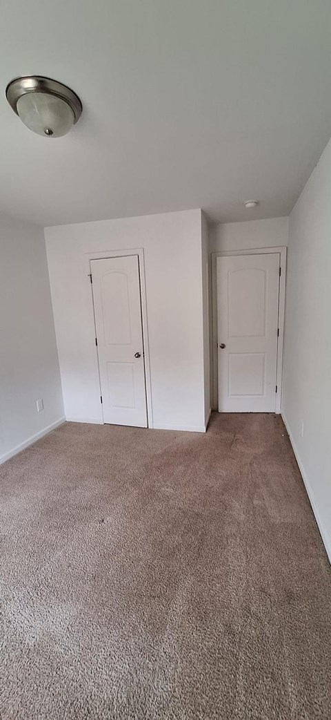 A room with white walls and carpeted floor with two doors.