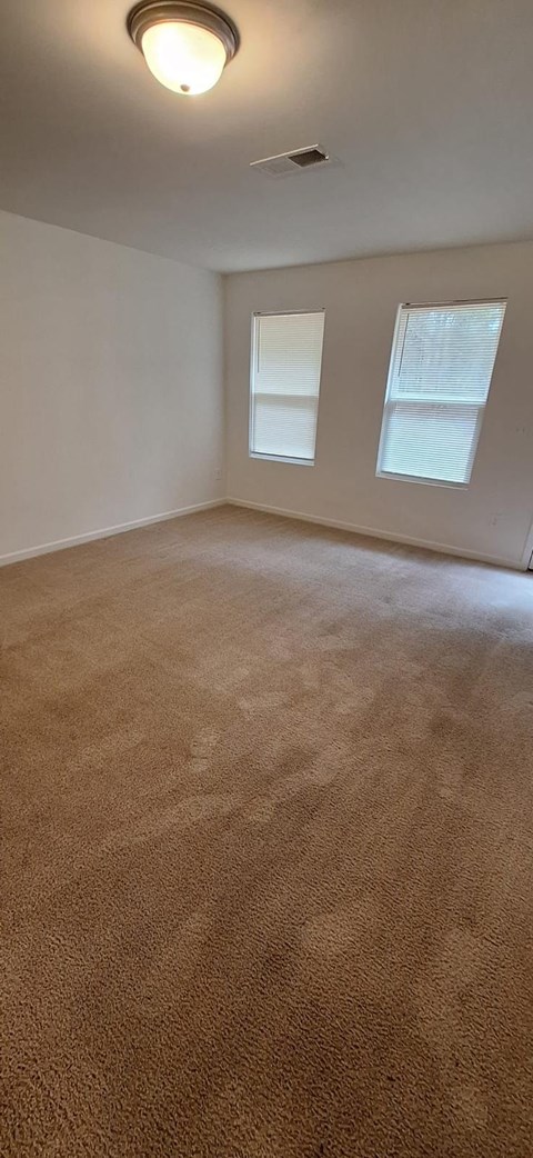A room with a carpeted floor and two windows.