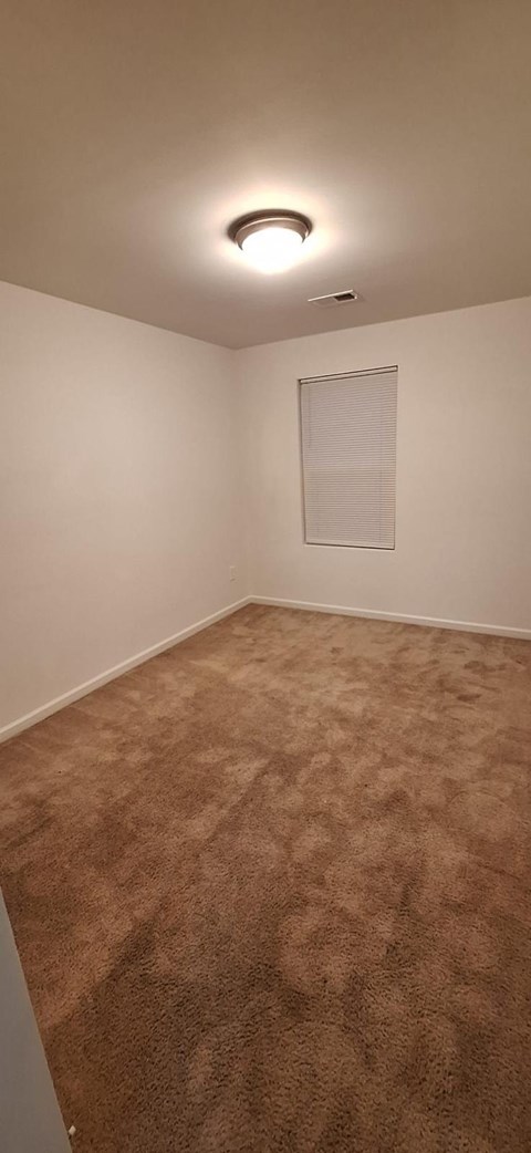 A room with a carpeted floor and a window with blinds.