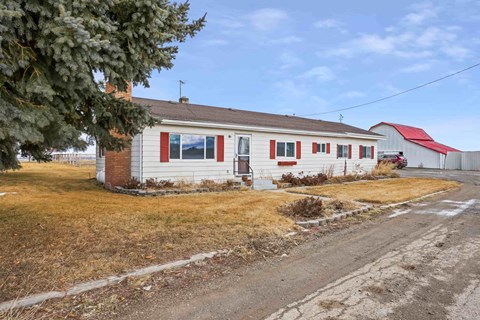 A house with a red roof and a white fence is surrounded by a grassy area.