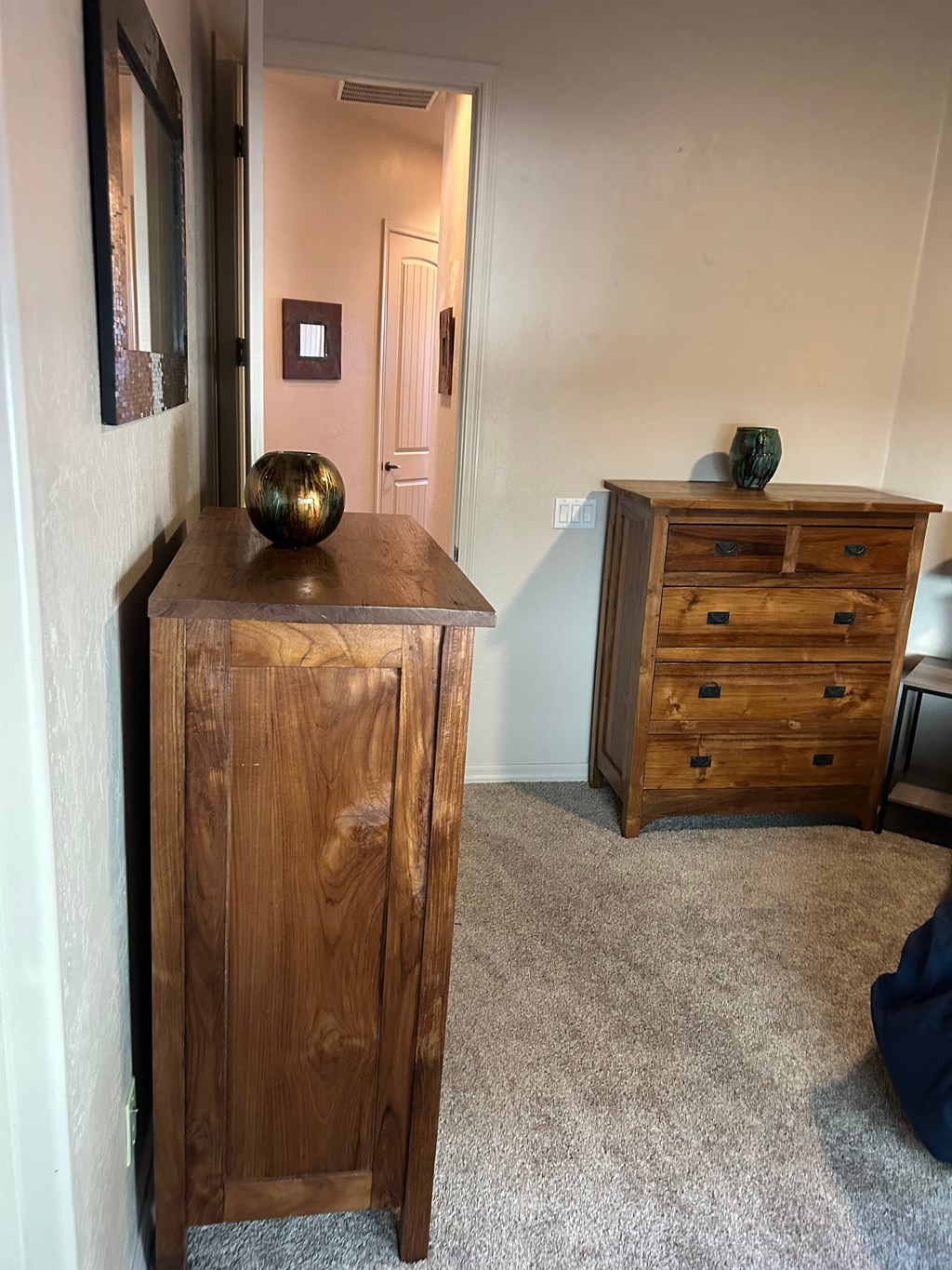 A wooden chest of drawers sits in a room with a carpeted floor.