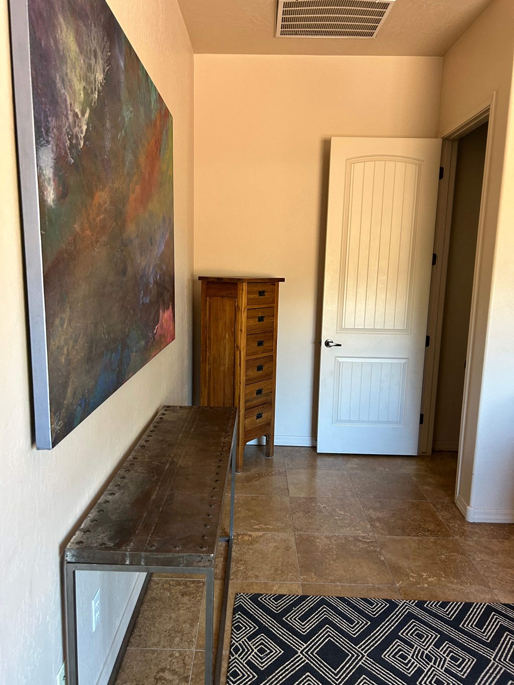 A painting hangs on a wall above a wooden cabinet and a table.