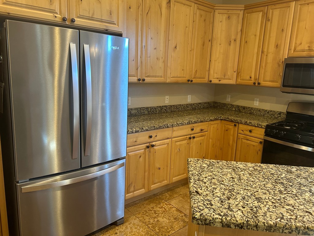 A stainless steel refrigerator stands in a kitchen with wooden cabinets.