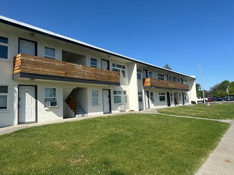A white building with a balcony and a green lawn in front.