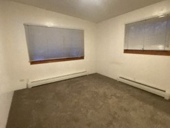 A room with a carpeted floor and two windows.