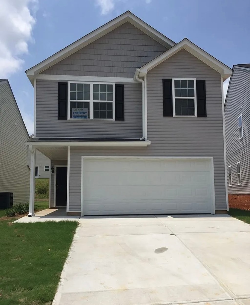 A two-story house with a garage door and a window with a sign that says "For Sale".