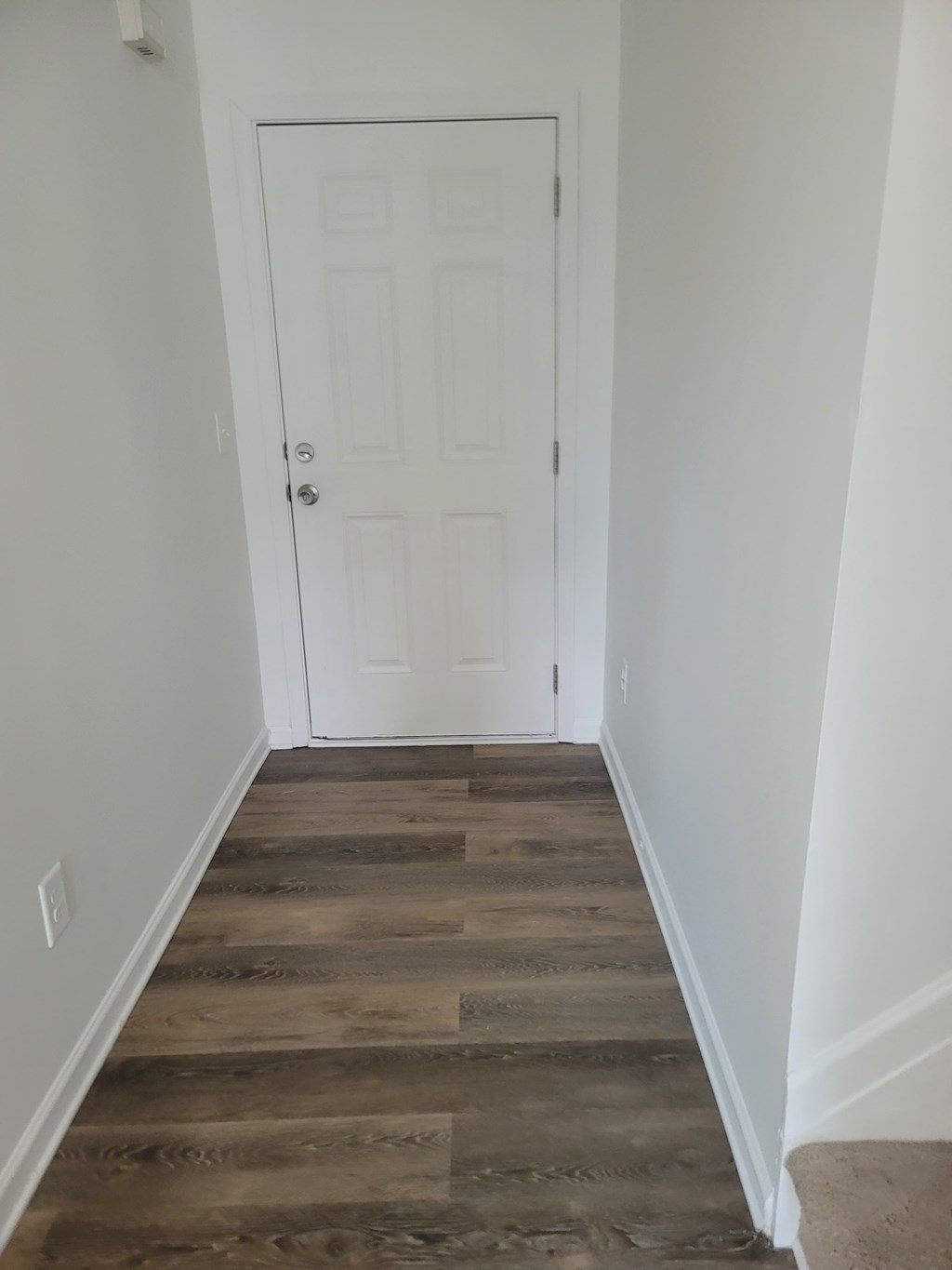 A white door is at the end of a hallway with wood flooring.