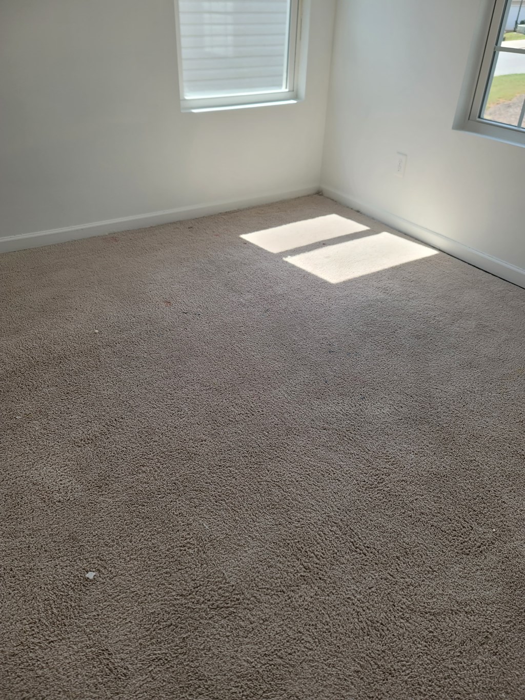 A room with a carpeted floor and a window letting in sunlight.