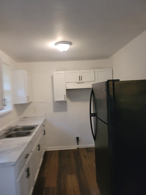 A black refrigerator in a kitchen with white cabinets.