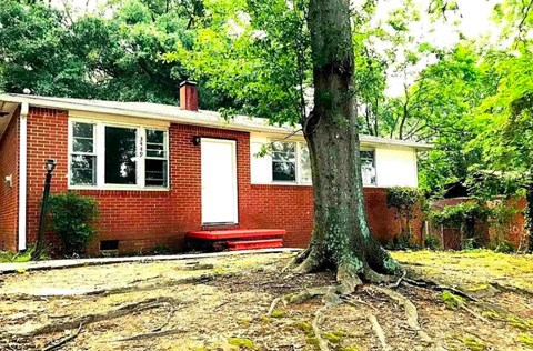 A red brick house with a white door and windows, surrounded by trees.