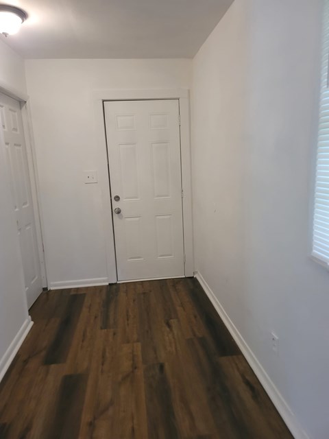 A white door is in the middle of a hallway with wood floors.