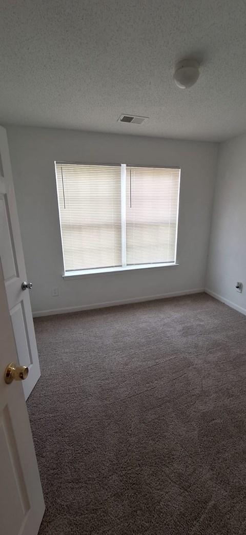 A room with a carpeted floor and a window with blinds.