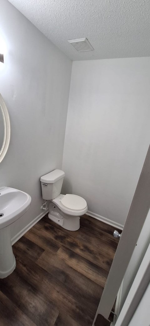 A white toilet sits in a small bathroom with wood flooring.