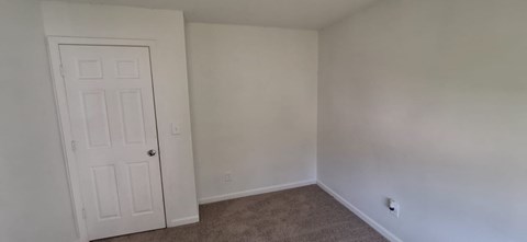 A white door is on the left of a room with a carpeted floor.