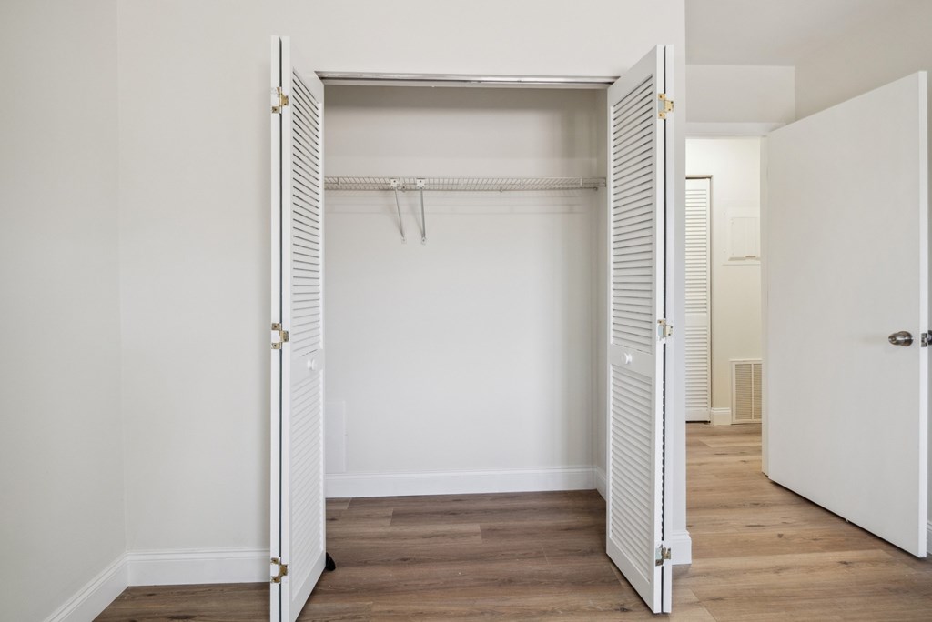 A white closet with a door open and a coat hanging on the rod.