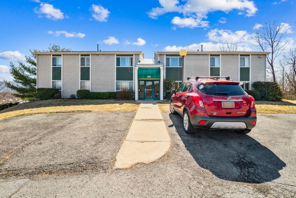 A red car is parked in front of a building with a green awning.