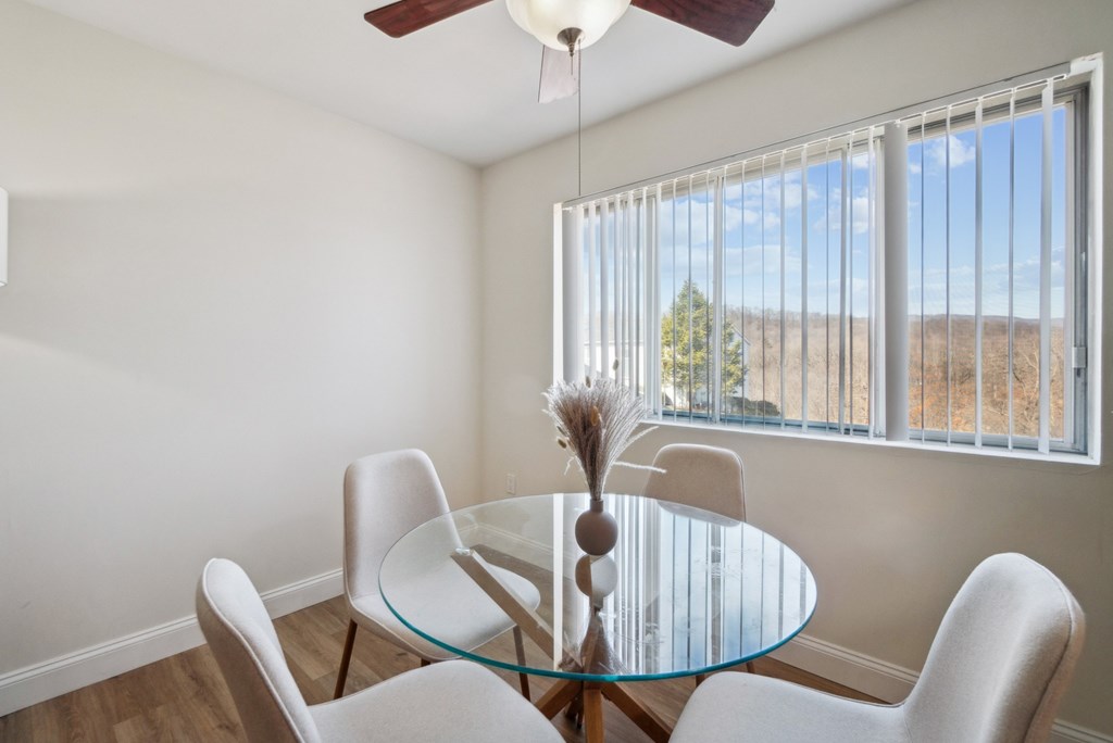 A glass table with four chairs and a fan in a room with a window.