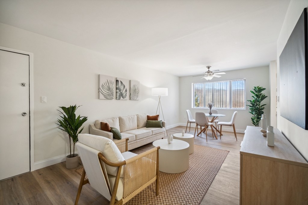 A living room with a white sofa, a wooden chair, and a TV on the wall.