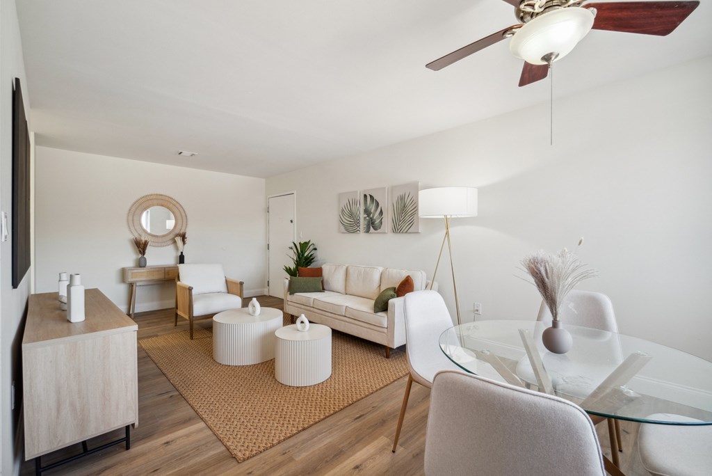 A living room with a white couch, a glass table, and a ceiling fan.