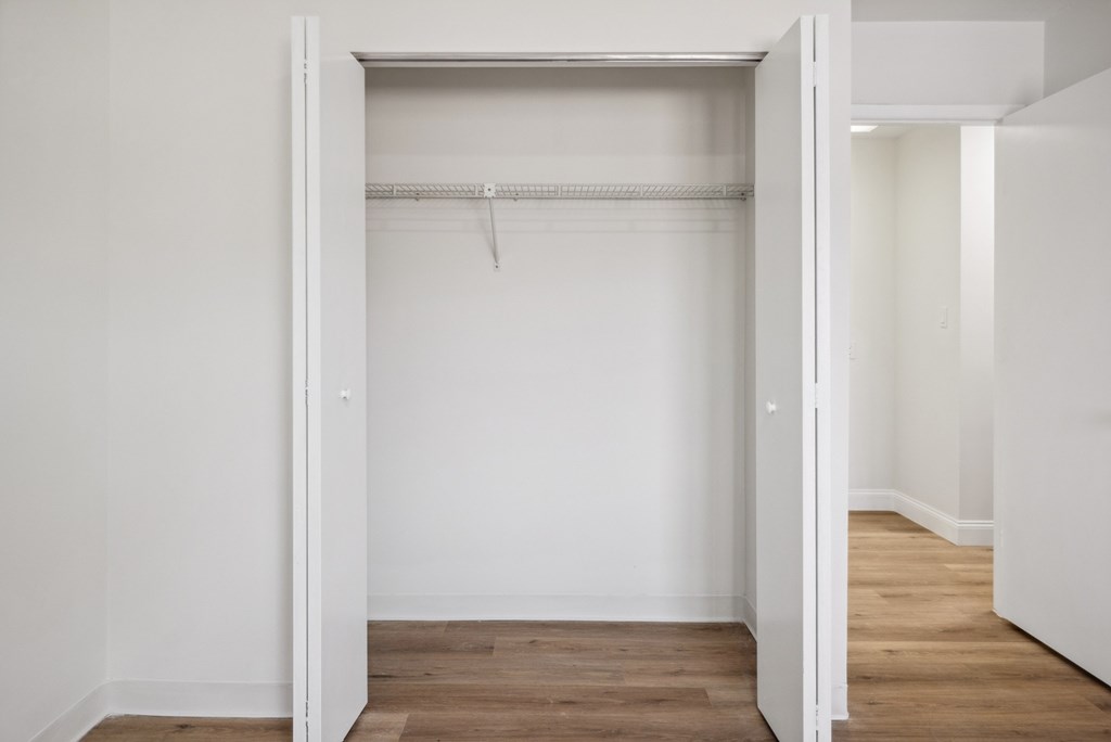 A white room with a wooden floor and a white closet with a hanger.