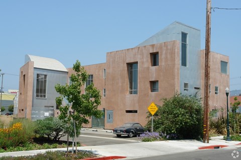 A modern building with a grey and brown exterior is surrounded by greenery and a street sign.